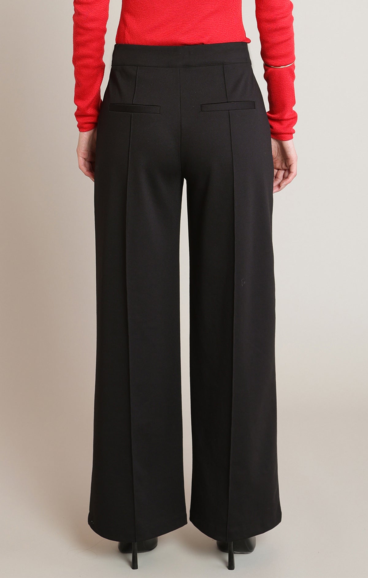 Black wide-leg pants worn with a red top on a beige background