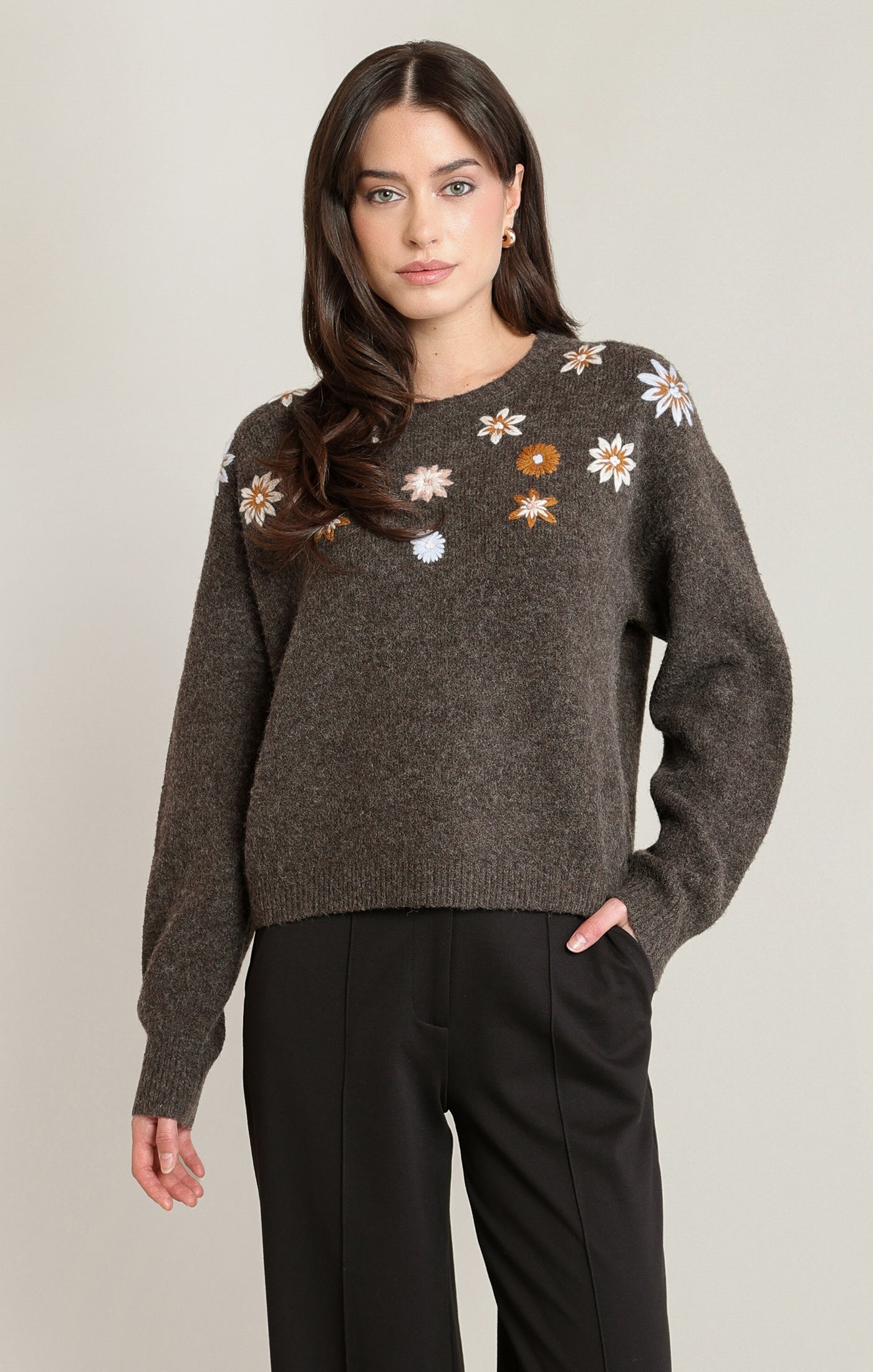 Woman wearing a dark gray sweater with floral patterns on a plain background