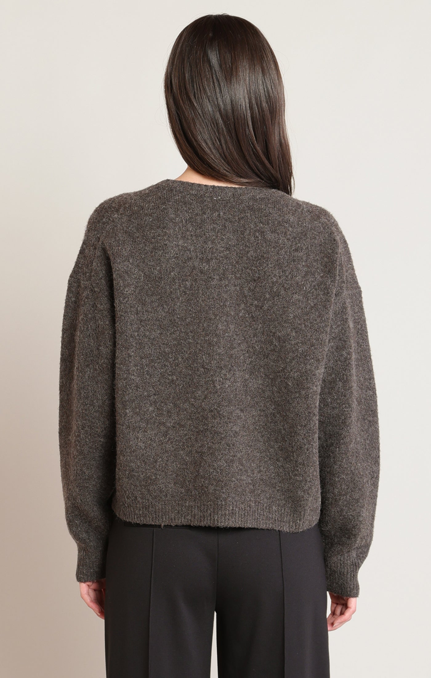 Person wearing a brown sweater from behind on a beige background