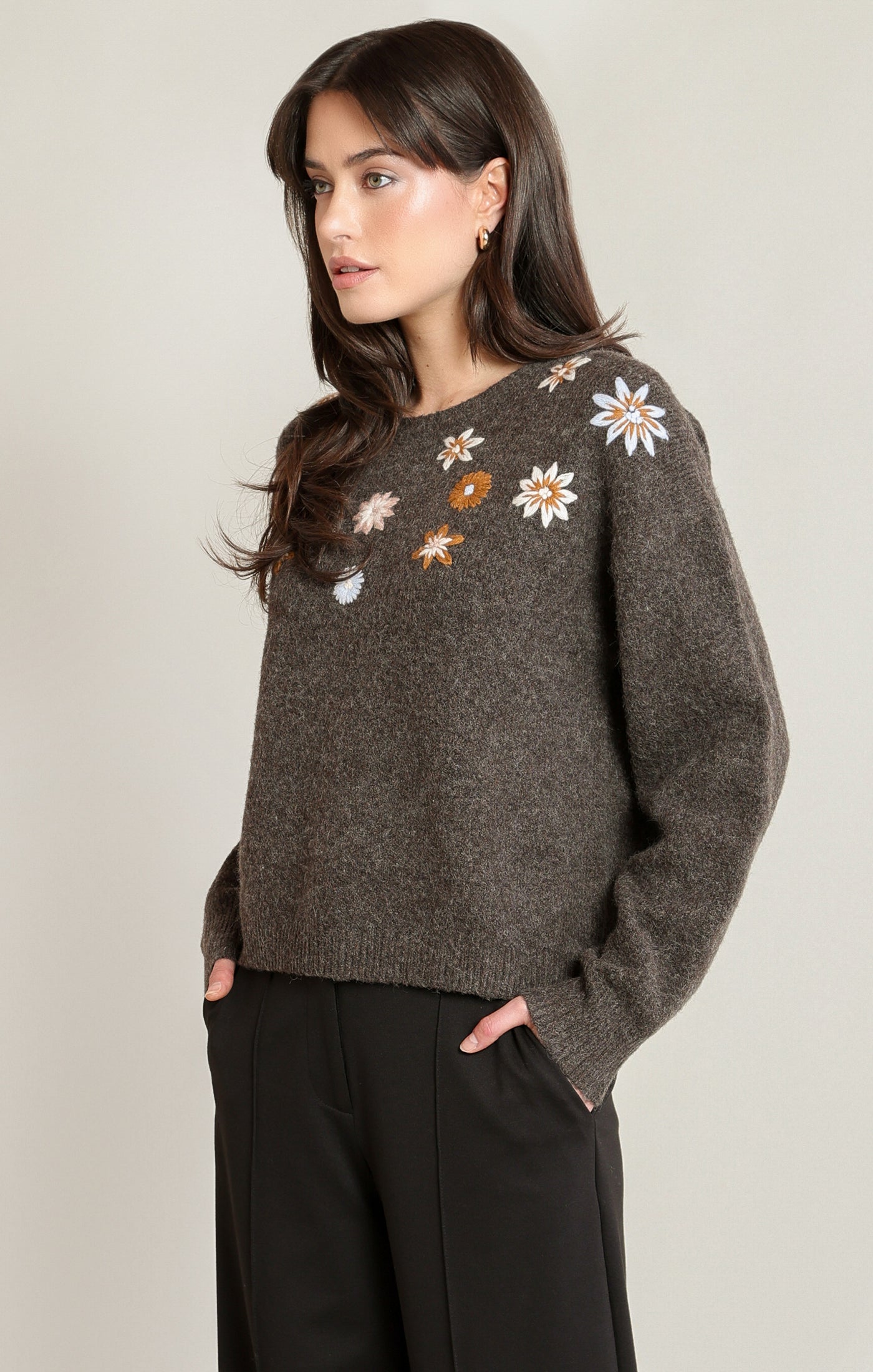 Woman wearing a brown sweater with floral patterns on a plain background