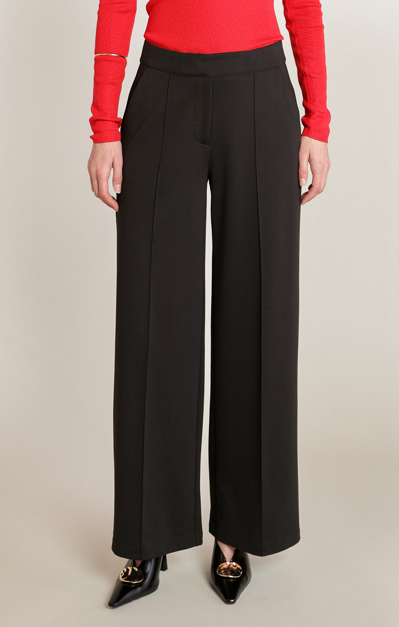 Person wearing black wide-leg pants with a red top on a beige background