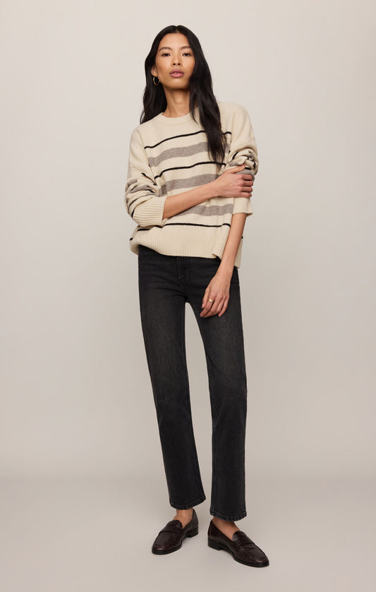 Woman wearing a striped sweater and black pants on a plain background