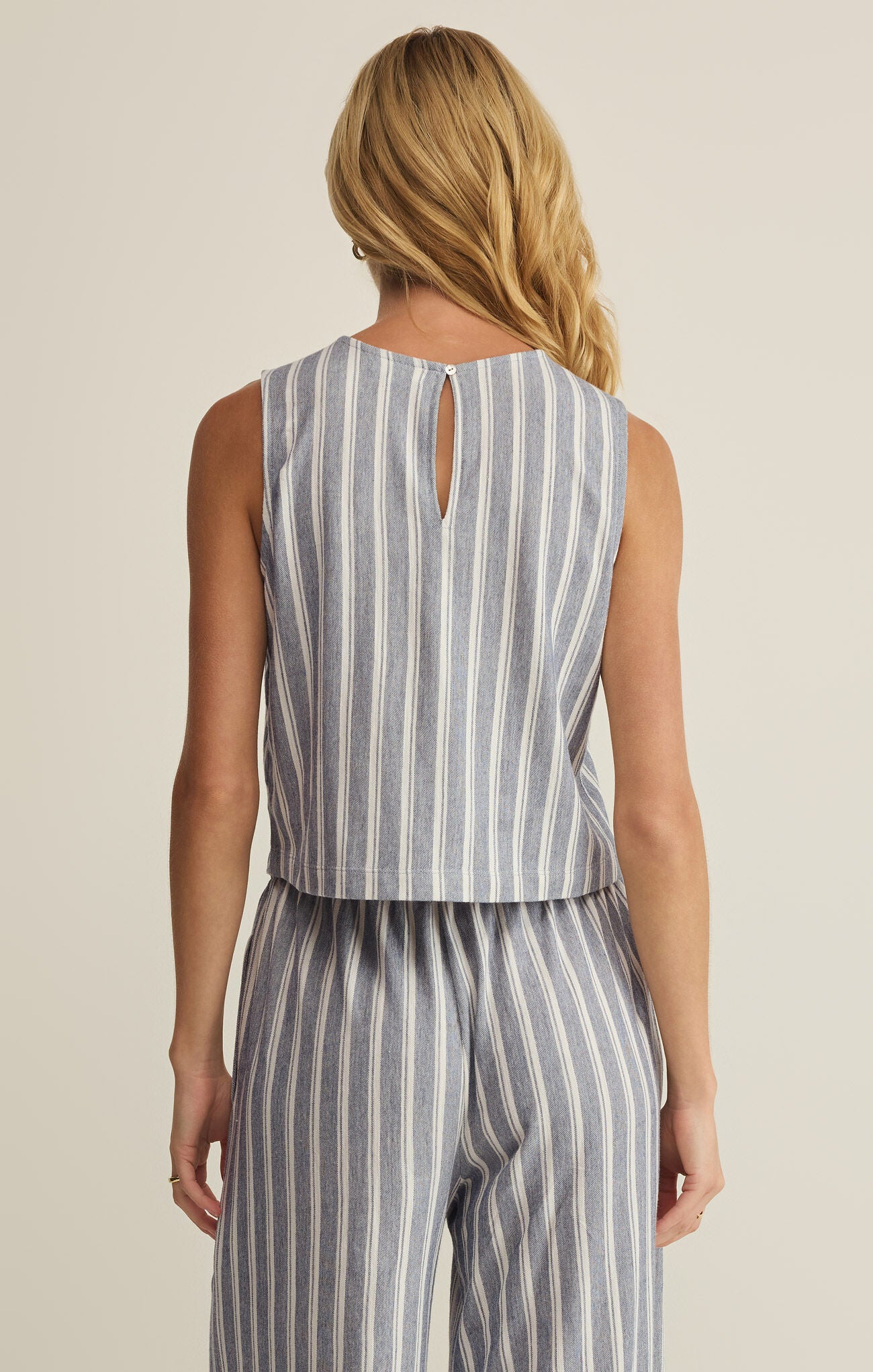 Woman wearing a sleeveless striped top and pants on a beige background