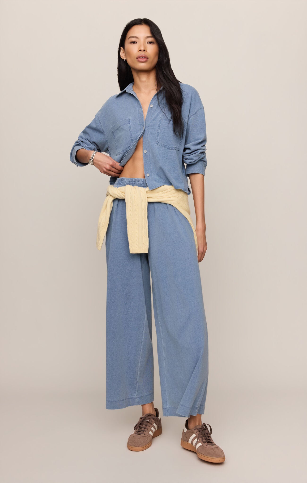 Woman wearing a blue shirt and pants with a beige apron on a beige background