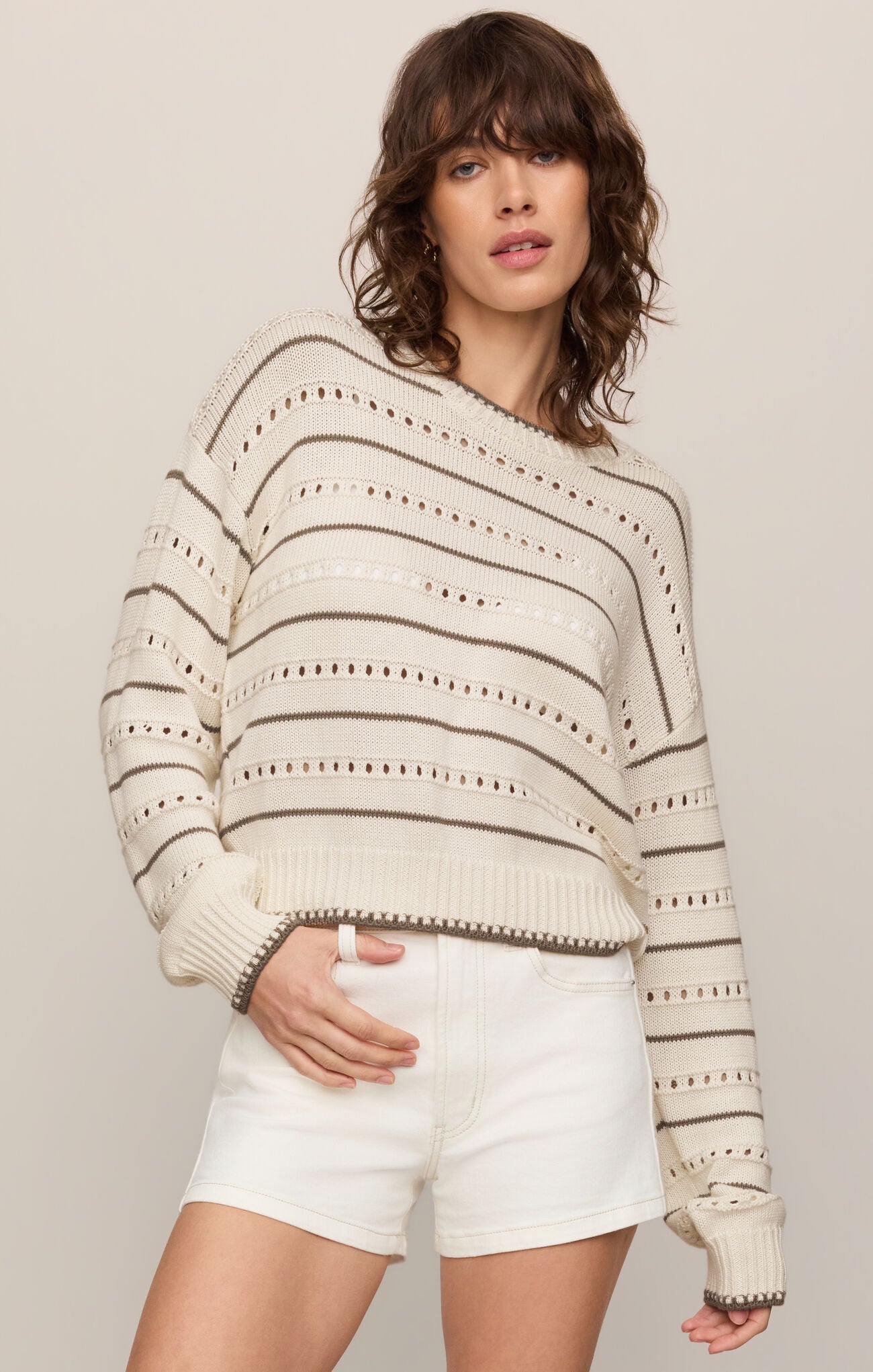 Woman wearing a striped sweater and white shorts against a plain background