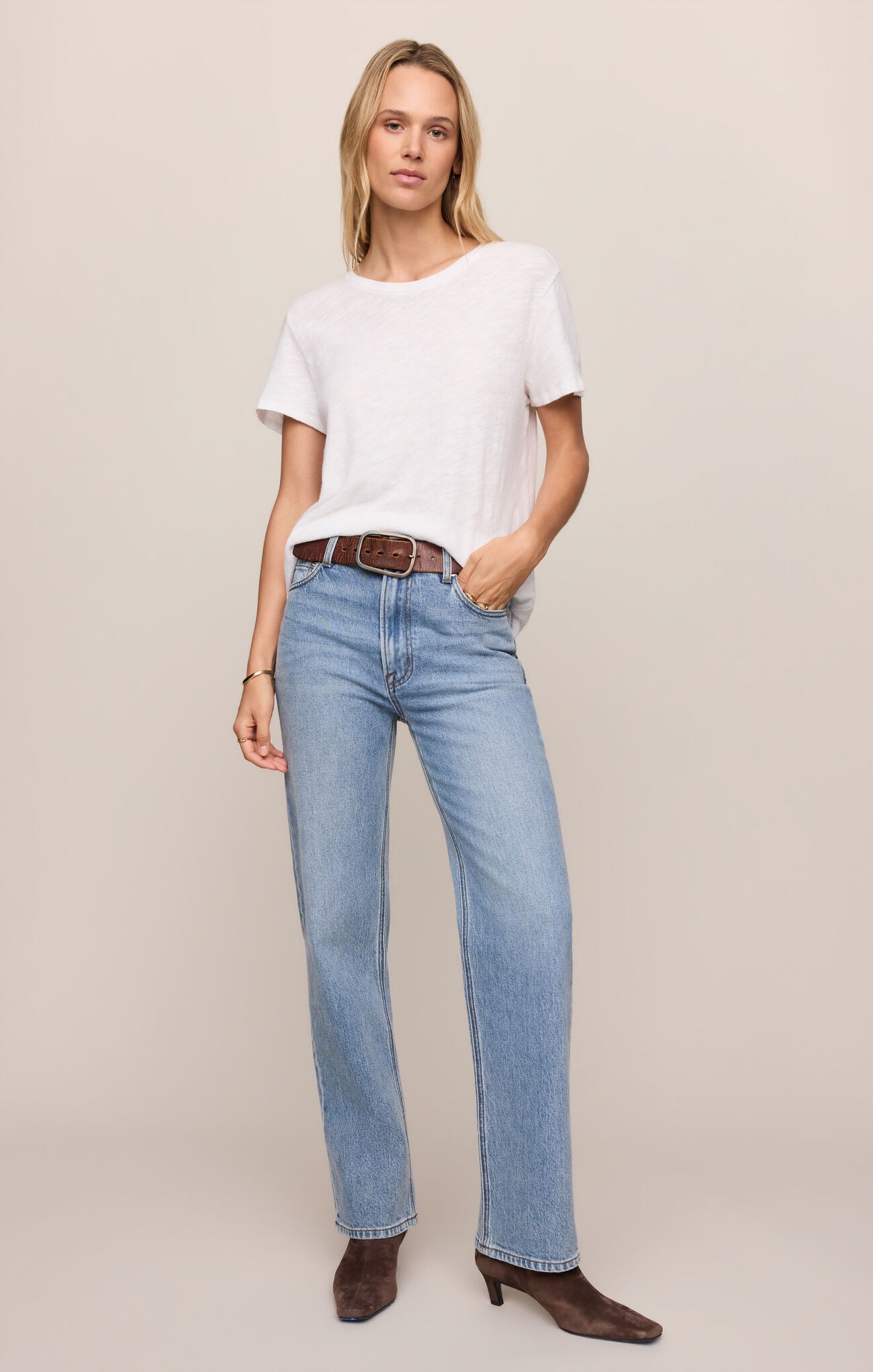Woman wearing a white t-shirt and blue jeans on a beige background